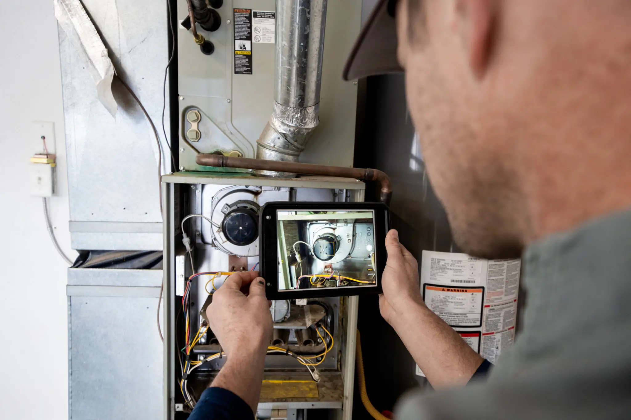Technician inspecting a furnace using a tablet for diagnostics.