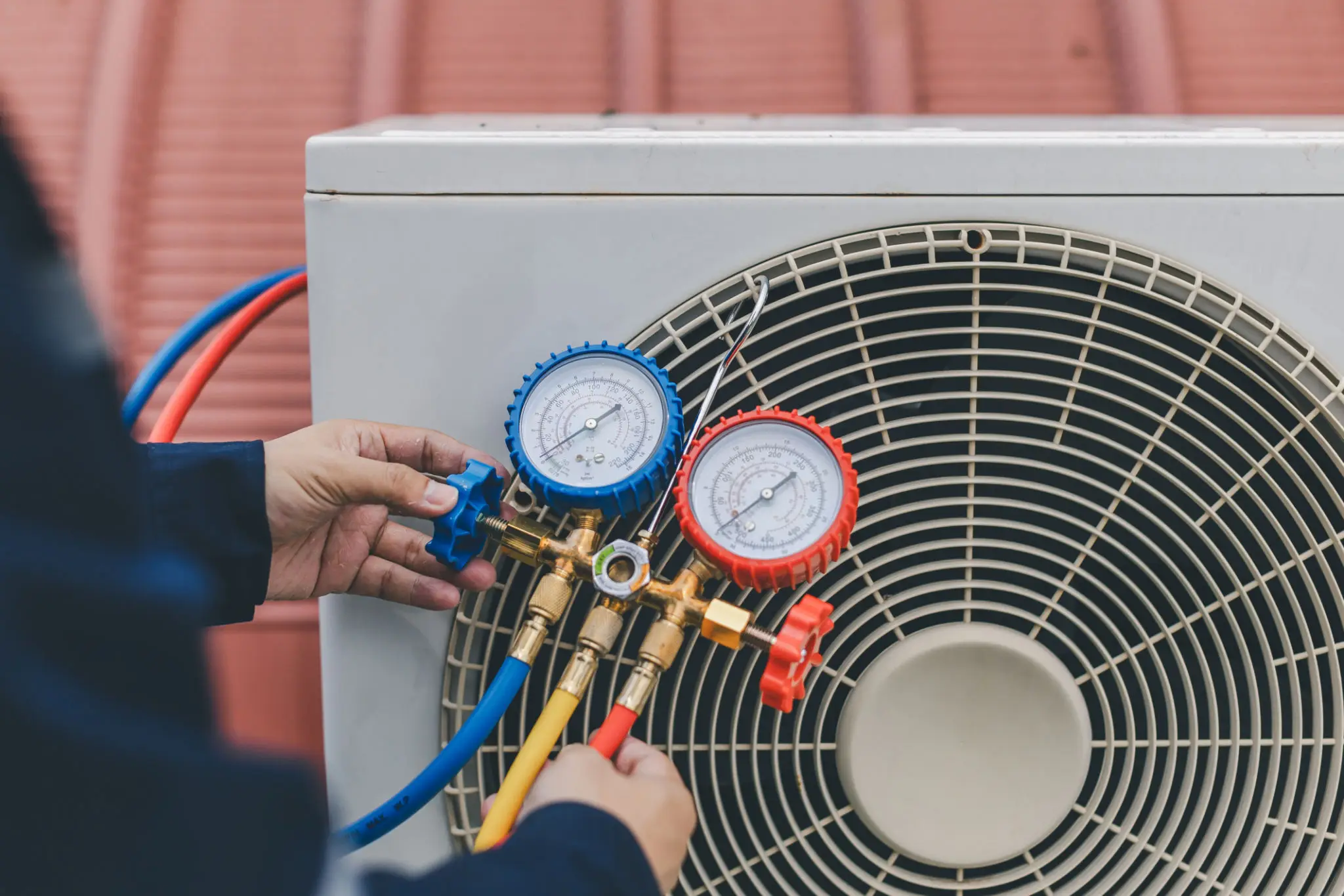 Technician adjusting HVAC gauges on an outdoor air conditioning unit.