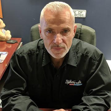 Man with gray hair sits at desk in office setting.