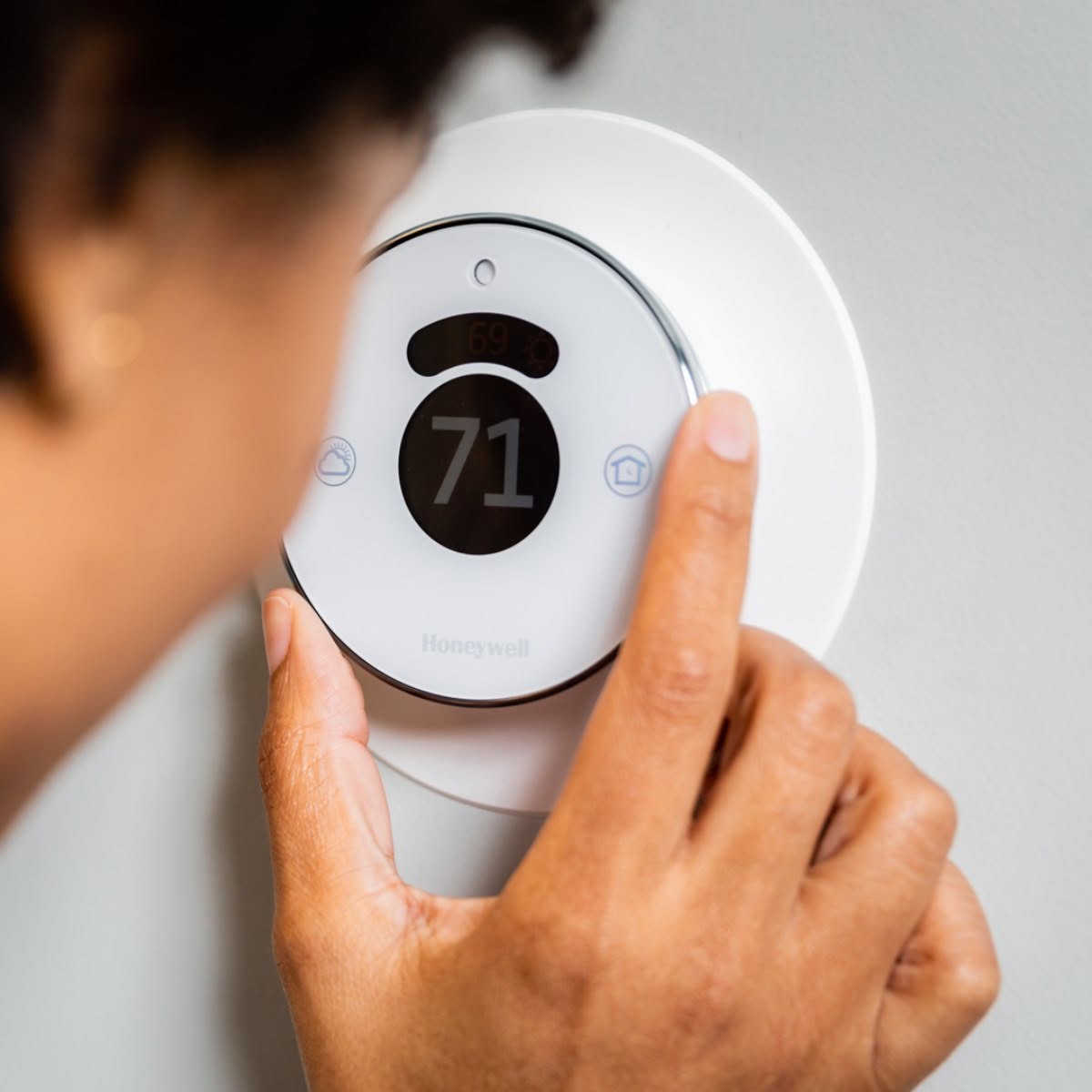 Homeowner adjusting a white Honeywell smart thermostat on a wall in Annapolis, MD.