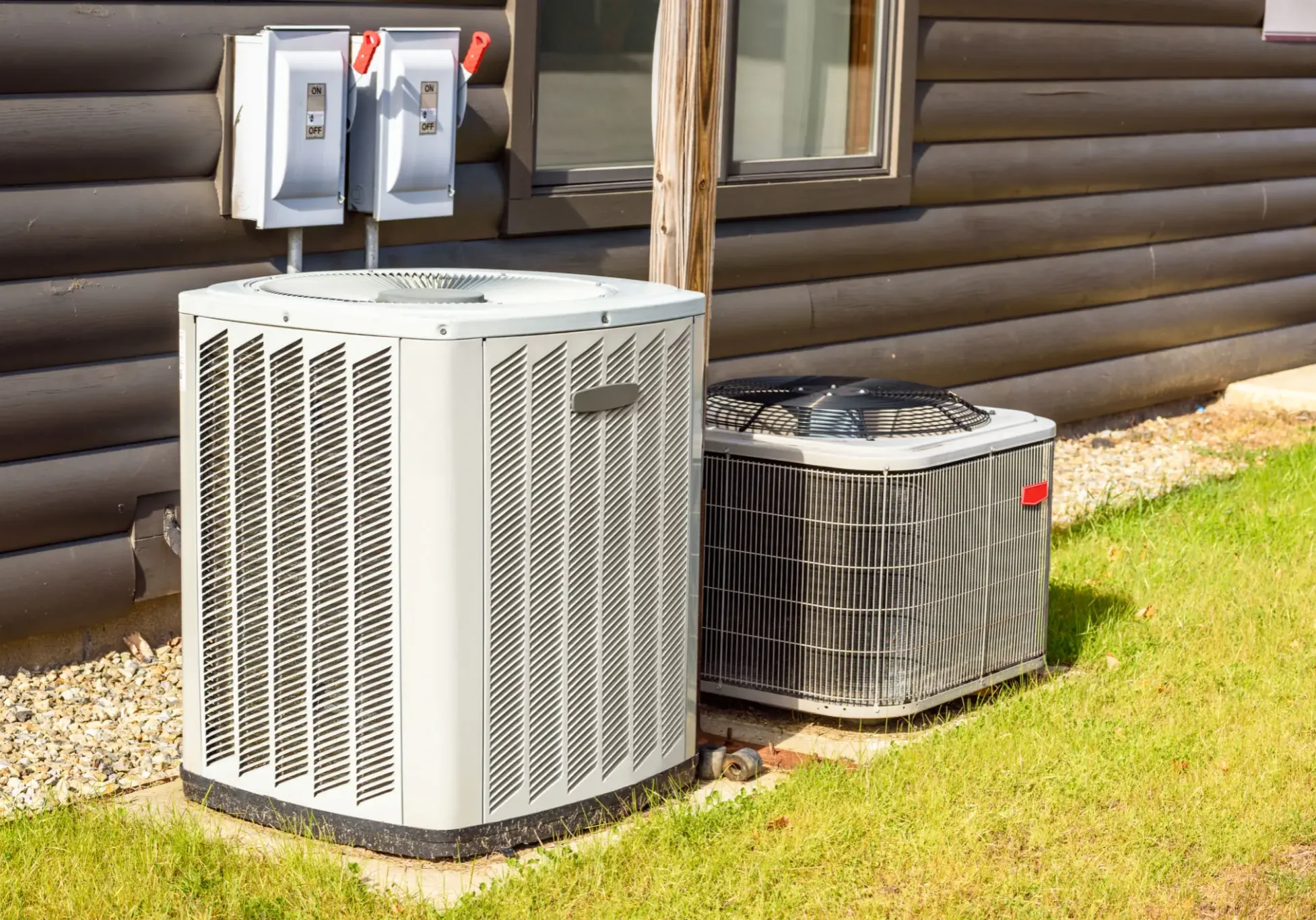 Two outdoor air conditioning units beside a log cabin.